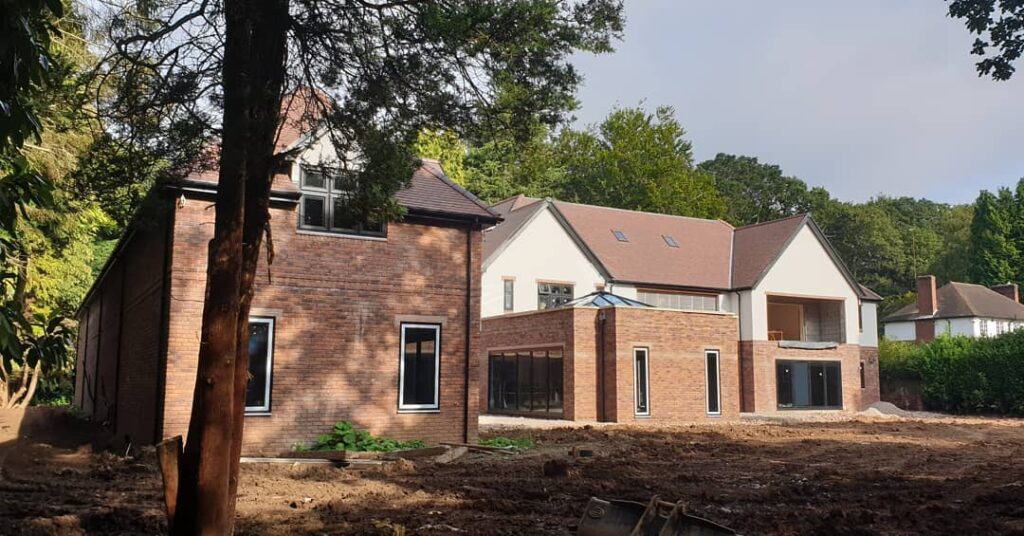 Modern brick new build house with garage in the building and exterior buildings with a tree in the foreground